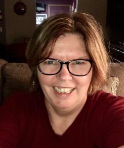 Anne Richter smiles for a photo in a dark room on the couch 